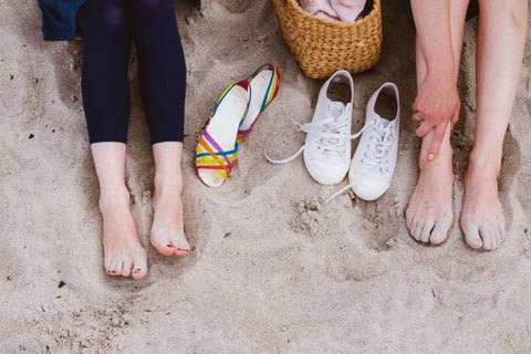 Zwei Personen sitzen barfuss im Sand, daneben Schuhe und ein Korb